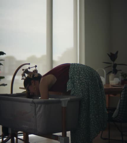 Mother attends a baby laying on a crib in a room near a window at home