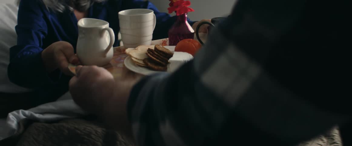 A male man handing off breakfast to a woman in bed