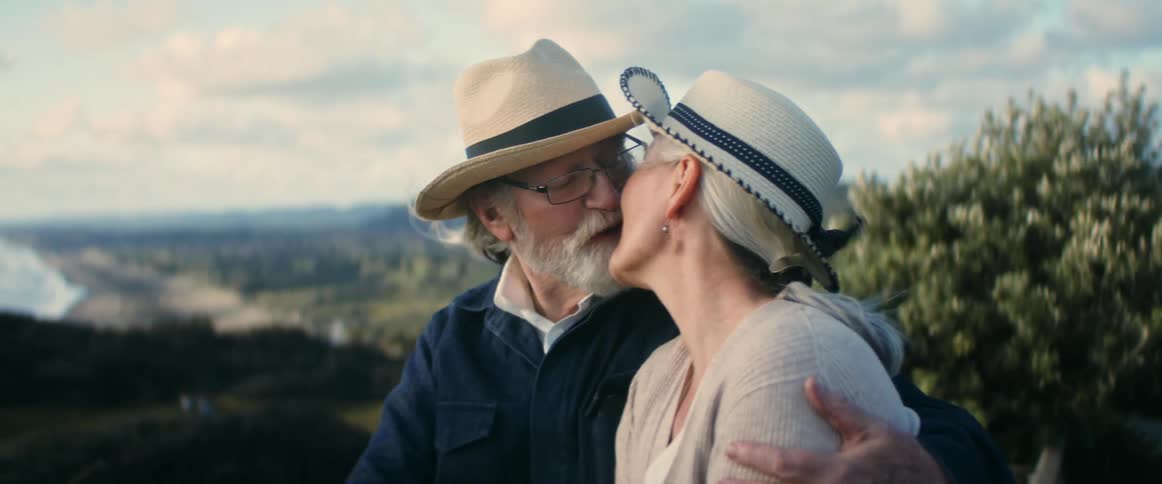 A man and woman sitting looking at each other sentimentally kissing and smiling