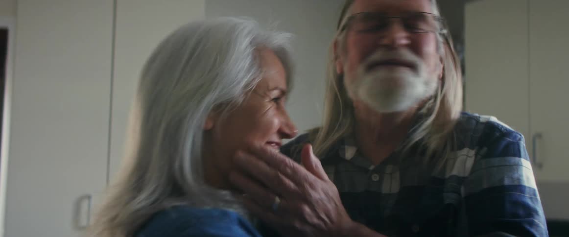 An elderly man and woman smiling and embracing indoors