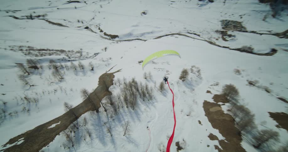 A paraglider wearing a parachute and skis flying through the air above a snowy landscape