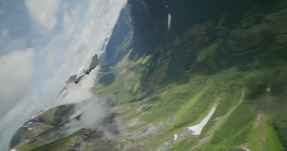 A person gliding and spinning in the air above lush green trees and a valley