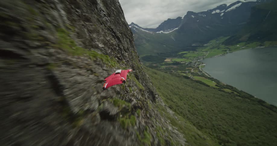 A person wearing a wingsuit jumps off a cliff and flies along the mountainside as they float down to the valley below