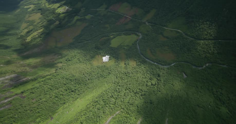 A person wearing a wingsuit is flying over a mountain valley