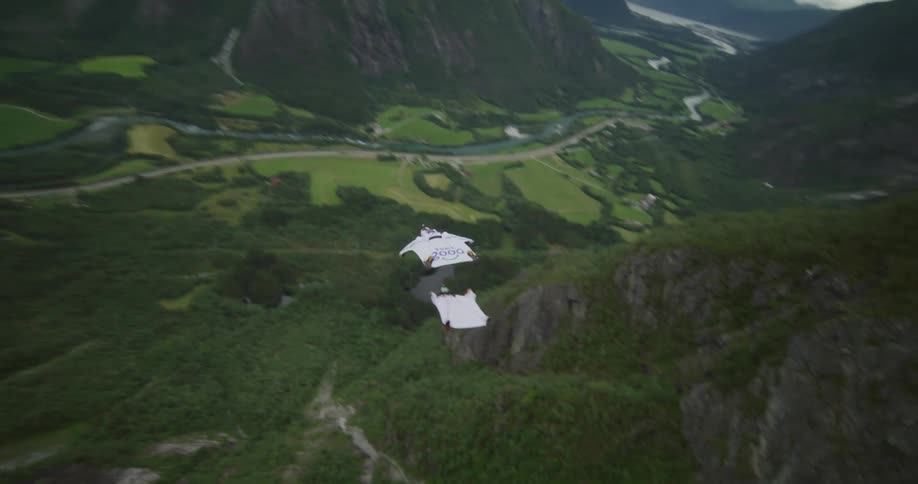 Two people jumping off a cliff and gliding down through a grassy valley