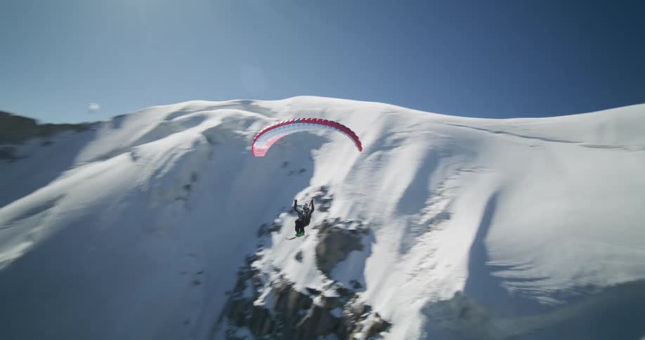 Ski glider jumps off slope and glides through air near mountain