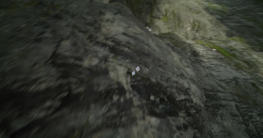 Two people wearing wingsuits are floating along the side of a mountain and over a mountain ravine