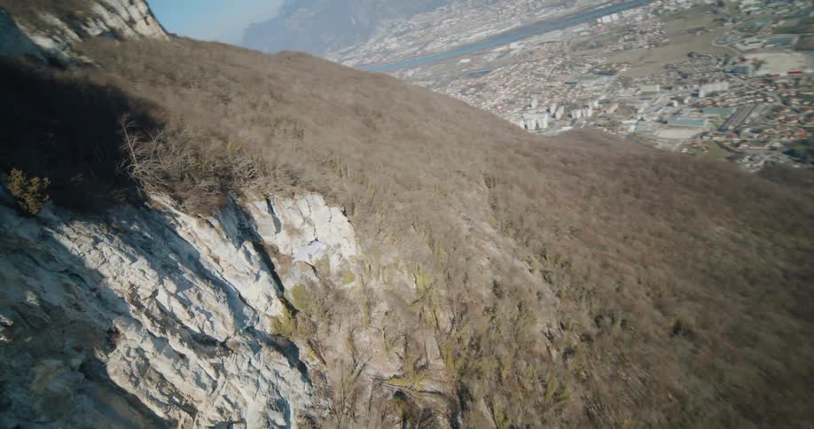 A person wearing a wingsuit jumps off a cliff and flies along the mountainside as they float toward the valley community below