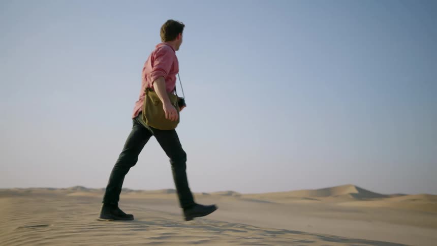 Man walks through the desert carrying a camera