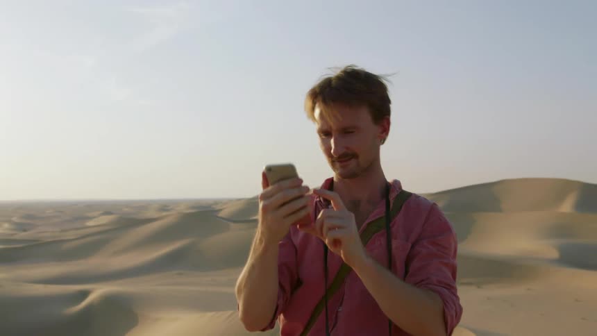 A man is holding up a phone in a desert