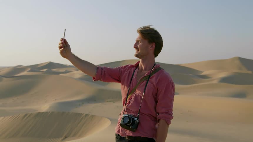 A man takes a photograph with his phone in the desert