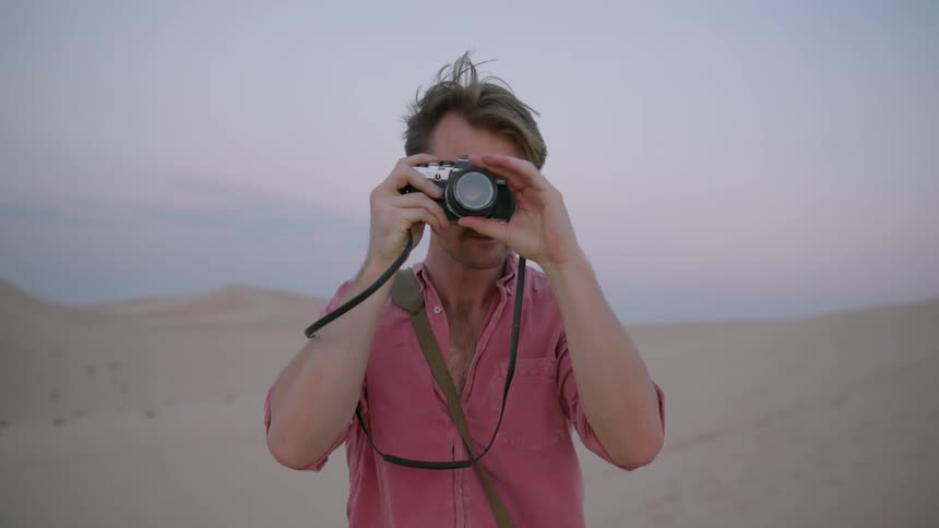 Man standing in a desolate sandy area while taking photographs