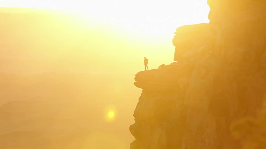 Silhouette of a man  standing on the edge of a cliff with the sun shining brightly behind