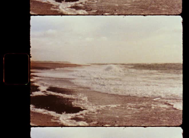 Powerful ocean waves washing ashore a sandy beach with white foam on the breaking waves while the water moves back and forth on the sandy shoreline on old film footage