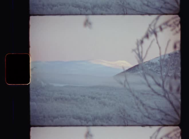 Sun rises and shines onto the peak of a snow-covered mountain in the background of a wide valley on a foggy or misty winter morning with snow and a clear blue sky as the landscape with bare icy trees is covered in ice due to freezing cold temperatures
