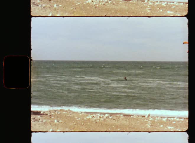 Retro Ws of rocky beach and a seaside boat onshore while a sporty or athletic person is windsurfing or kite surfing on the ocean waves enjoying the outdoor activities during summer vacation in the 1980s