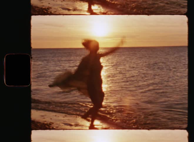 Silhouette of unrecognisable young woman in a light summer dress twirling and dancing in a happy and carefree way on a beach as the sun sets over the ocean or sea at the horizon expressing happiness or high spirits and joy