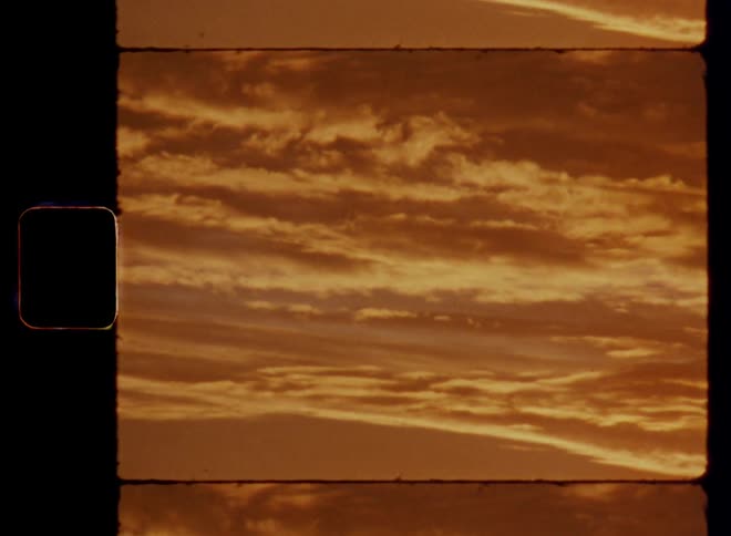 Wide vintage Super 8mm aerial shot of a cloudy sky with vibrant sepia and red tones during sunset