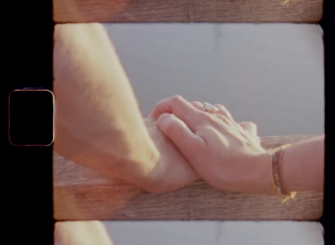 Romantic Super 8 mm film footage of a woman laying her hand on the hand of a man that is placed on the railing of a pier next to a lake during a date as the sun sets on a warm summer evening