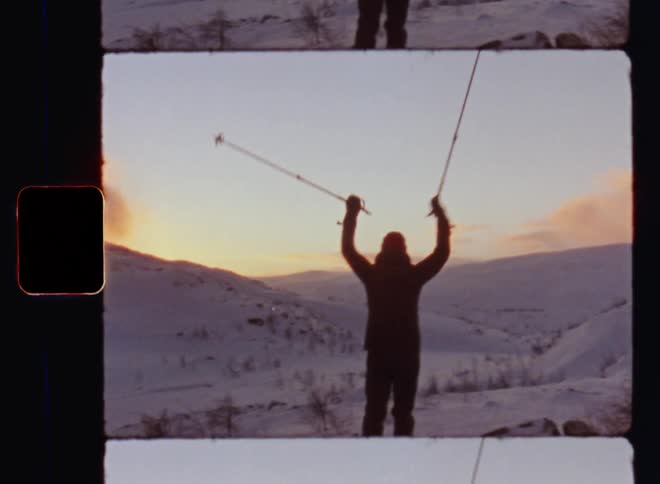 Handheld dynamic 8mm film footage of a female woman athlete raising ski poles above her head looking out over a snow covered mountain range expressing happiness and gratitude for a great outdoor adventure in the evening light with glowing clouds