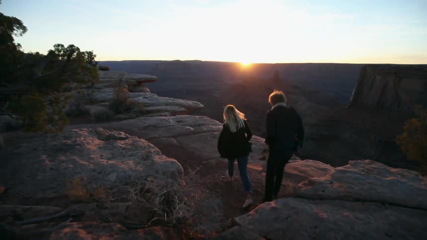 Two people are walking along the top of a mountain near the cliff