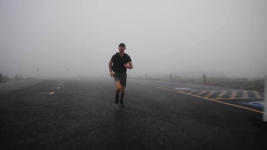 A man exercises as he runs down a foggy street