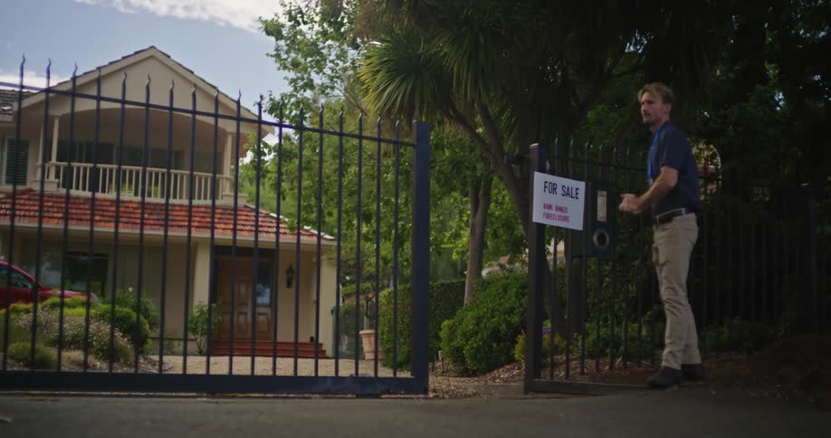 Man walks out of closing house gate and hangs for sale sign on fence