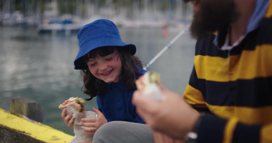 Father and daughter are eating while they do some fishing