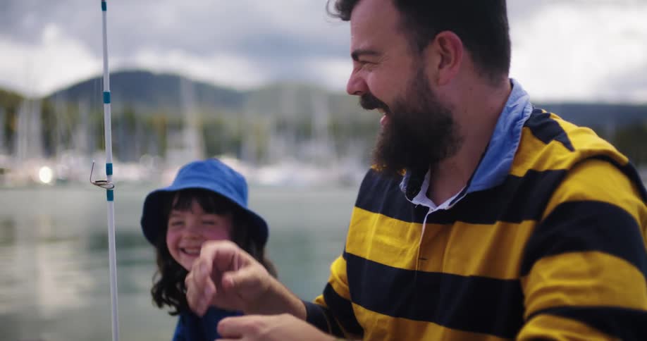 A man is fishing with his young daughter and teasing her as he baits the hook