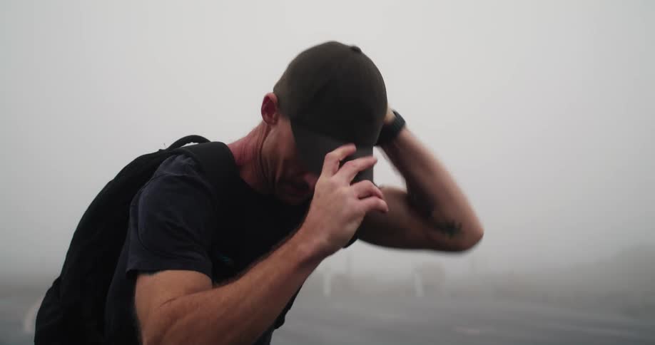 Man with cap dark blue shirt and backpack runs on highway in fog