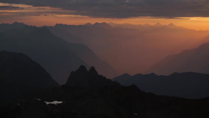 The sun sets behind a mountain range on a cloudy evening
