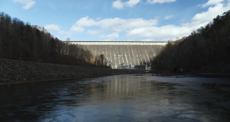 Drone flies low over stream and pans up to a dam