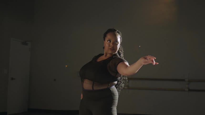 Woman with curly hair black shirt and leggings dances in dance studio
