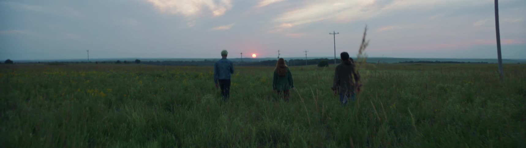 A group of people walking through a rural grassy field at sunset
