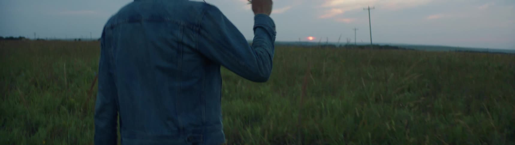 A man putting on a pair of glasses while walking in a meadow at sunset