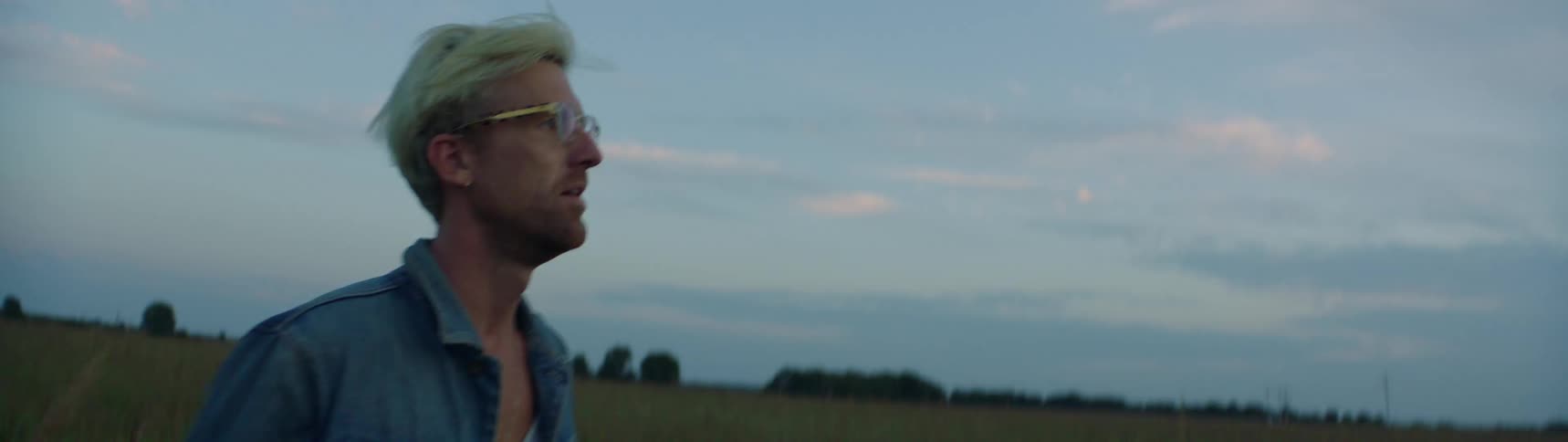 Blonde man walks across field under a cloudy sky