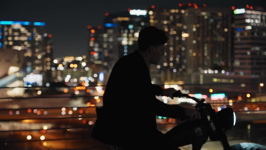 A man riding a bicycle in a city at night and stopping to enjoy the view