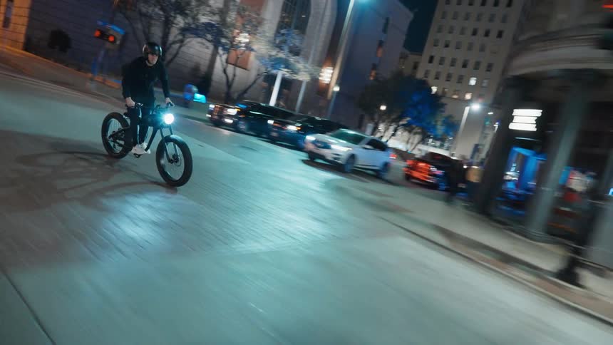 A man is riding a bike through a downtown city at night
