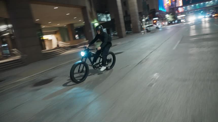 A person drives a bicycle on an empty road in the city at night