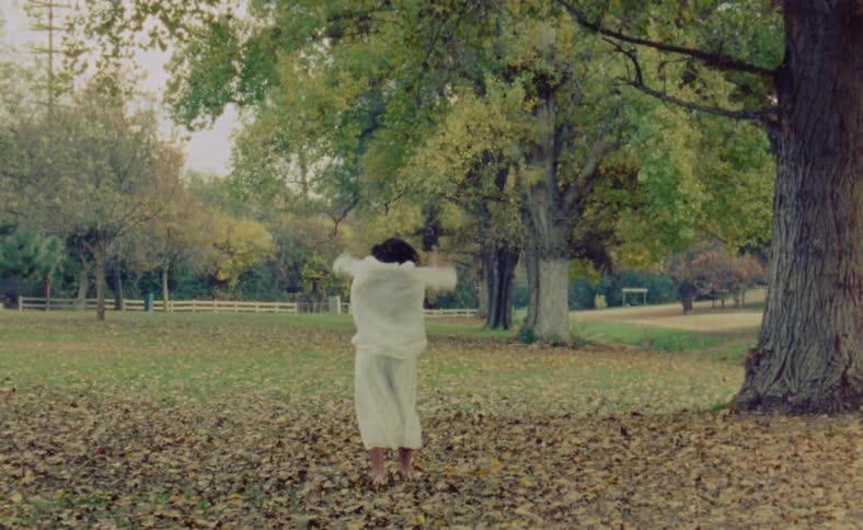 A man moving erratically dancing and moving his arms while under a large tree