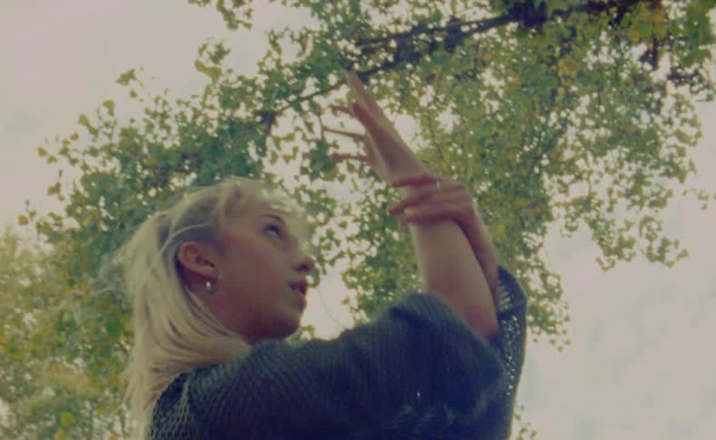 A woman is doing aggressive dance movements outside under a tree