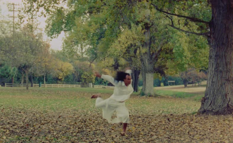 A man is doing interpretive dance movements outside in a field