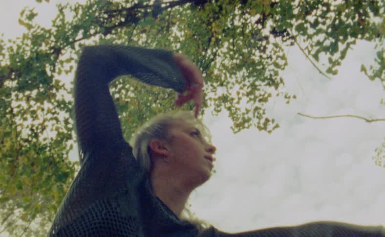 A woman is dancing outdoors near a tree