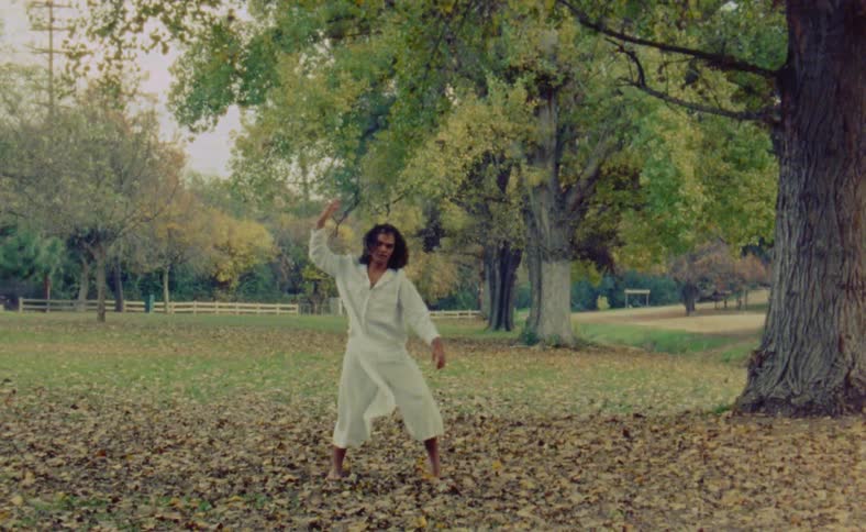 A man is dancing outdoors in a field of grass and leaves