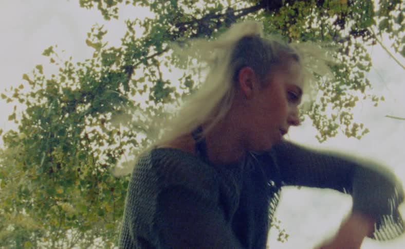 A woman is dancing outdoors next to a tree