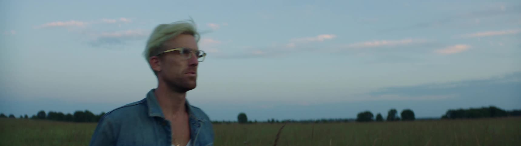 A man is walking through a grassland area at dusk