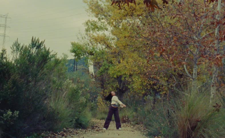 Woman dances on path near trees in their fall foliage with powerlines in the background