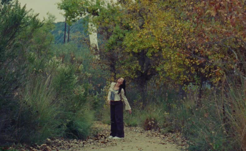 A woman is doing dance movements outside in between trees