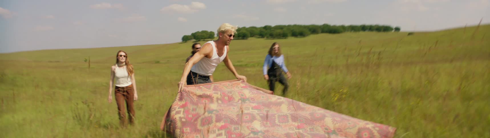 A group of friends lay a large blanket down in a field