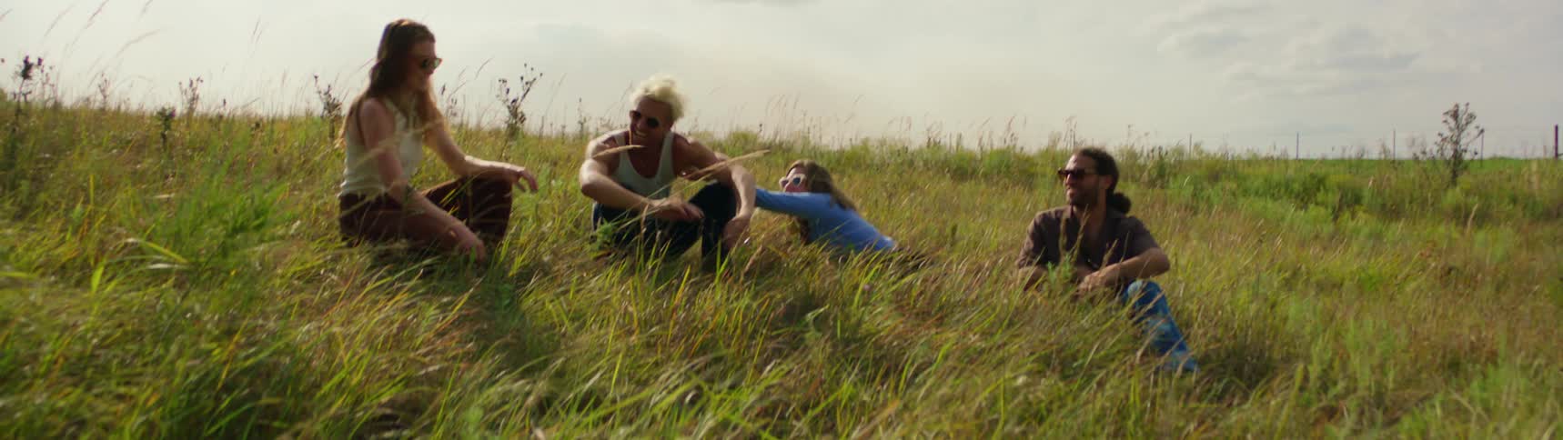 Friends play while sitting in grass in field on a cloudy day